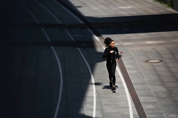 High angle view of african american woman in black sportswear running on track — Stock Photo