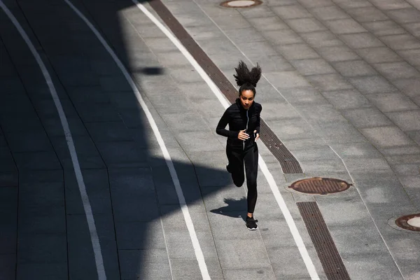 Vista de ángulo alto de la deportista afroamericana en chaqueta deportiva corriendo en pista — Stock Photo