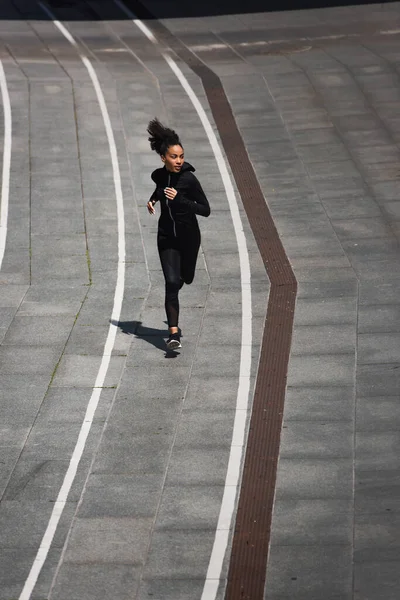 Pretty african american sportswoman running on track outdoors — Stock Photo