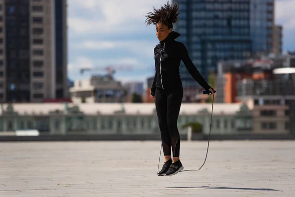 Sportiva afroamericana che salta con la corda sulla strada urbana — Foto stock