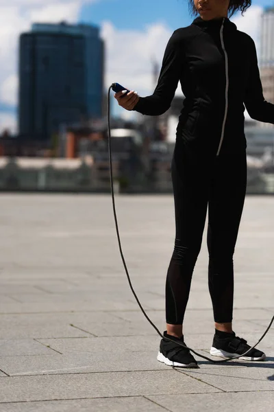 Cropped view of african american sportswoman holding jump rope on urban street — Stock Photo