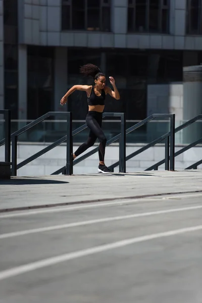 African american sportswoman running near railing on urban street — Stock Photo