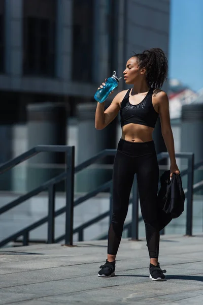 Vue latérale d'une sportive afro-américaine dans l'eau potable de la rue urbaine — Photo de stock