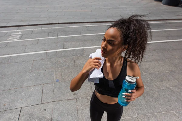 Высокий угол зрения на африканскую американку в спортивной одежде держа спортивную бутылку и полотенце на открытом воздухе — стоковое фото