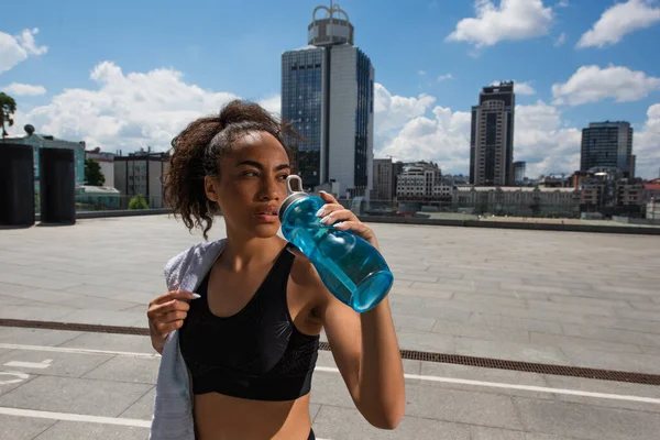 African american sportswoman holding towel and drinking water outdoors — Stock Photo