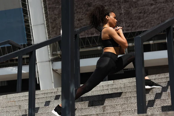 Vue latérale d'une sportive afro-américaine faisant des bonds dans les escaliers d'une rue urbaine — Photo de stock