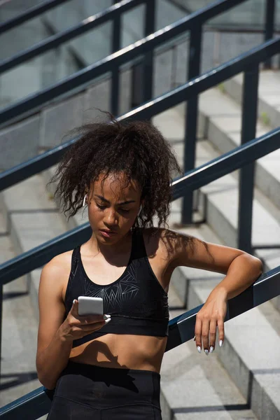 African american sportswoman in earphones using smartphone outdoors — Stock Photo
