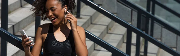 Веселая африканская спортсменка слушает музыку в наушниках на лестнице, баннер — стоковое фото