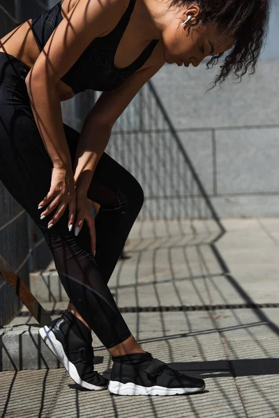 Side view of african american sportswoman in earphone restring near fence — Stock Photo