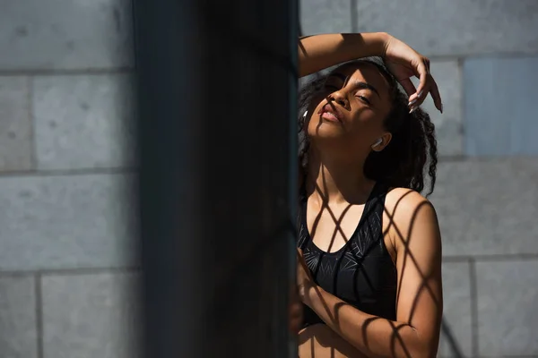 African american sportswoman in earphones looking at camera near fence outdoors — Stock Photo