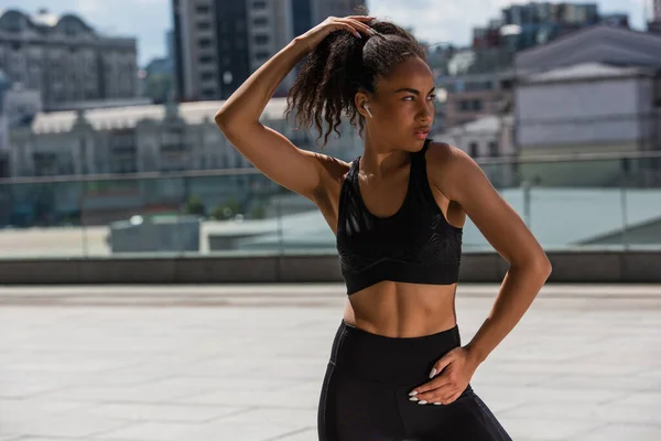 Young african american sportswoman in earphone looking away on urban street — Stock Photo