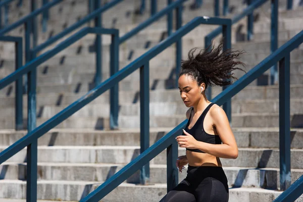 Fit african american sportswoman in earphone running on stairs — Stock Photo