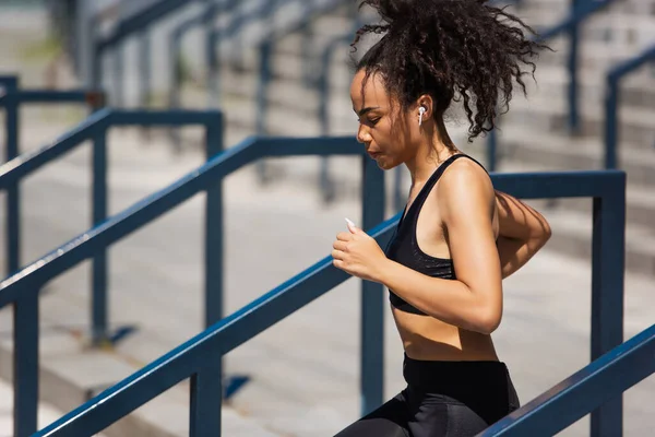 Side view of african american woman using earphone while running outdoors — Stock Photo