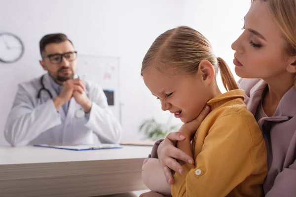 Krankes Kind berührt Hals nahe Mutter und verwischt Kinderarzt — Stockfoto