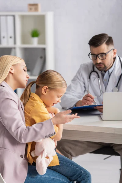 Mother looking at diseased kid near pediatrician on blurred background — Stock Photo