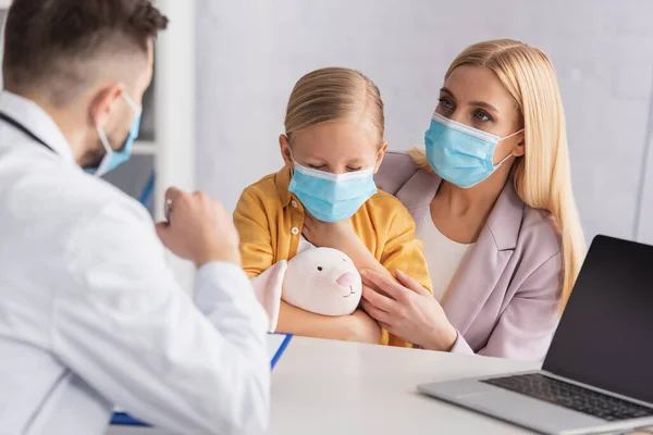 Sick girl holding soft toy near mother in medical mask and doctor — Stock Photo