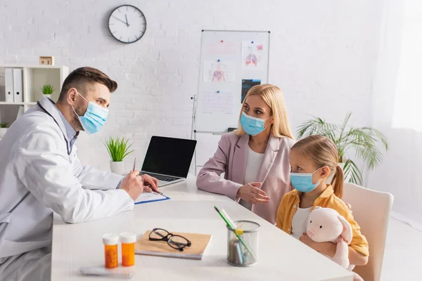 Woman pointing at child in medical mask near doctor in hospital — Stock Photo