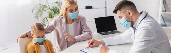Mother in protective mask pointing at kid near pediatrician writing on clipboard, banner — Stock Photo
