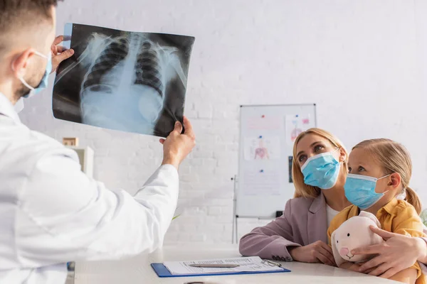 Doctor holding fluorography near mother and kid in medical masks in clinic — Stock Photo