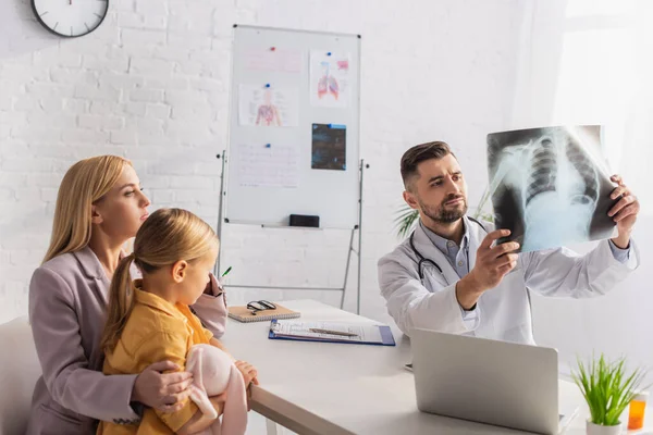 Pédiatre regardant la fluorographie près de la famille et ordinateur portable dans la clinique — Photo de stock