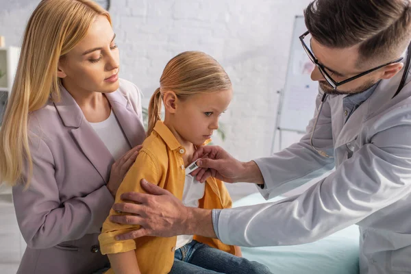 Medico di famiglia che tiene il termometro vicino a bambino e madre — Foto stock