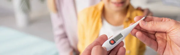 Cropped view of doctor holding thermometer near blurred patient and woman, banner — Stock Photo