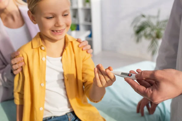 Doctor holding thermometer near positive kid on blurred background in hospital — Stock Photo