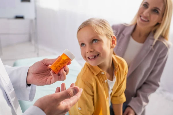 Педіатр тримає таблетки біля усміхненої матері і пацієнта на розмитому тлі — стокове фото
