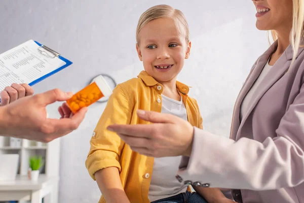 Médico con portapapeles sosteniendo pastillas cerca de la madre y el niño sonrientes - foto de stock