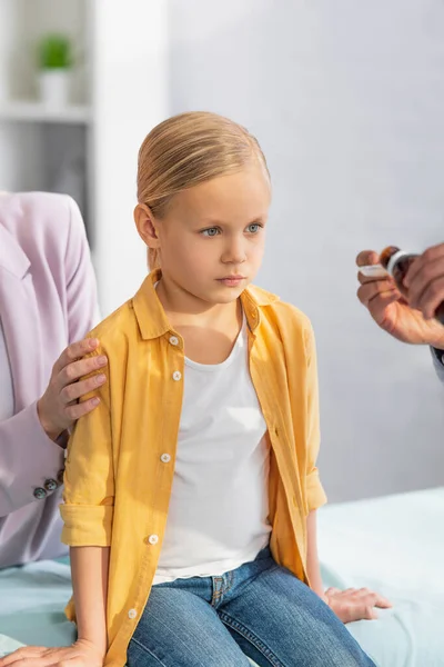Niño mirando borrosa médico de familia con jarabe cerca de la madre en el hospital - foto de stock