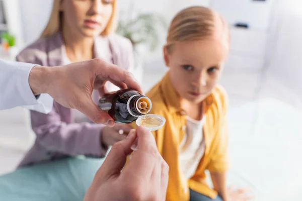 Pediatrician pouring syrup near blurred mother and child in hospital — Stock Photo