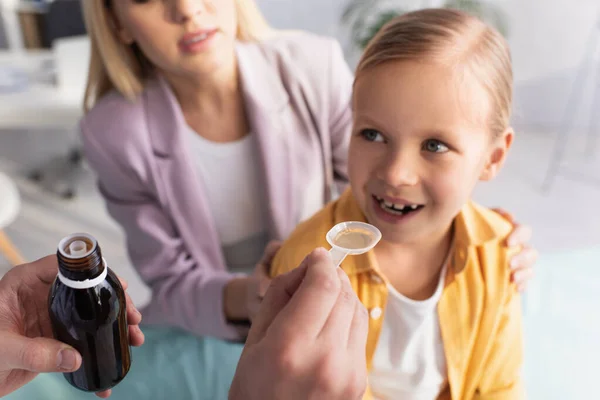 Doctor holding syrup near smiling girl and parent on blurred background — Stock Photo