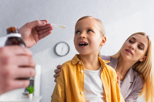 Pediatrician holding syrup near woman hugging kid in clinic — Stock Photo