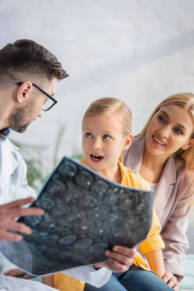 Niño asombrado mirando al médico de familia con resonancia magnética cerca de la madre sonriente - foto de stock