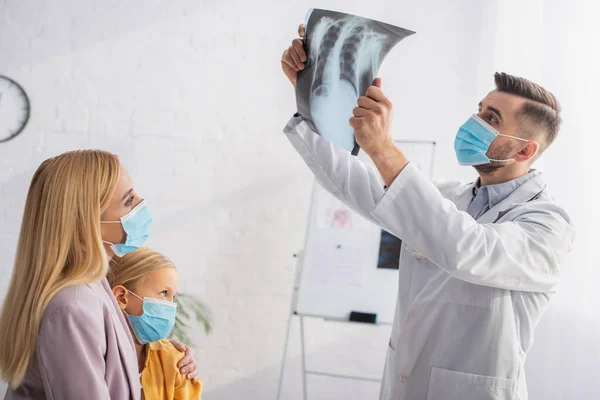 Kinderarzt in medizinischer Maske betrachtet Fluorographie in der Nähe von Mutter und Patient — Stockfoto
