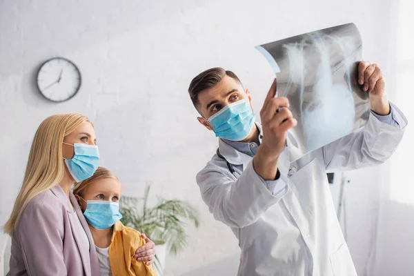 Woman in medical mask embracing kid near family doctor with fluorography — Stock Photo