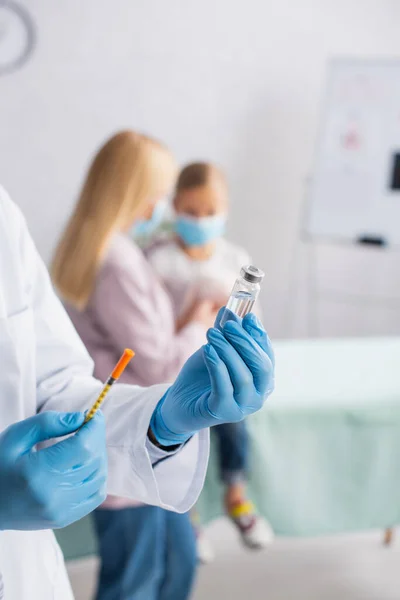 Pediatrician holding vaccine and syringe near blurred mother and kid — Stock Photo