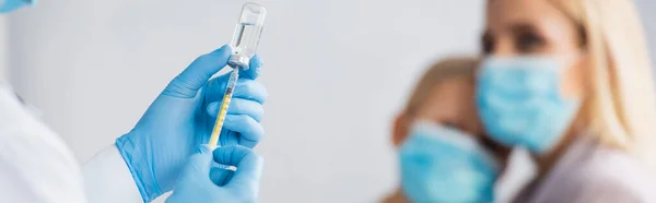 Pediatrician in latex gloves picking up vaccine near blurred mother and kid, banner — Stock Photo