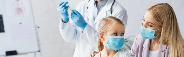 Mutter und Kind in Arztmasken neben verschwommenem Hausarzt mit Impfstoff, Transparent — Stockfoto