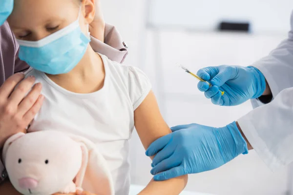 Pediatrician holding syringe near kid and parent in clinic — Stock Photo