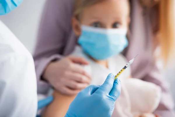 Médecin tenant une seringue près d'un enfant et d'une femme sur fond flou — Photo de stock