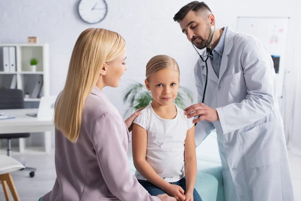 Mother looking at kid on medical couch near doctor with stethoscope — Stock Photo