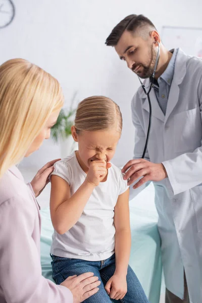 Kid sneezing near mother and doctor with stethoscope — Stock Photo