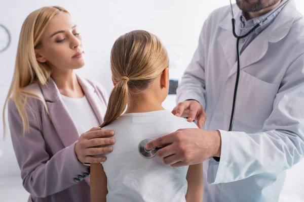 Pediatra usando estetoscopio en la espalda del niño en la clínica - foto de stock