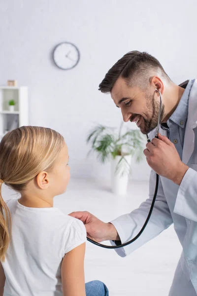 Веселый педиатр осматривает ребенка со стетоскопом в больнице — стоковое фото