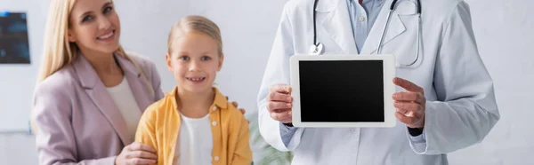 Medico con tablet digitale vicino a madre e bambino sfocati in clinica, banner — Foto stock