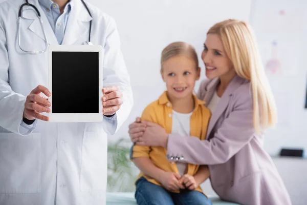 Doctor holding digital tablet near mother hugging kid in hospital — Stock Photo
