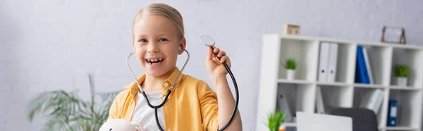 Niño feliz con juguete suave y estetoscopio en el hospital, pancarta - foto de stock