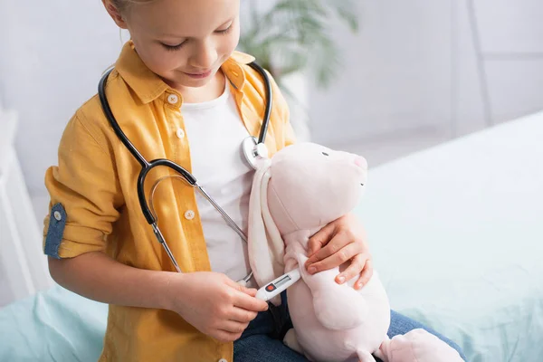 Menina brincando com brinquedo e termômetro eletrônico no hospital — Fotografia de Stock