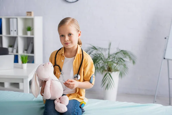 Child holding toy, thermometer and stethoscope on medical couch — Stock Photo